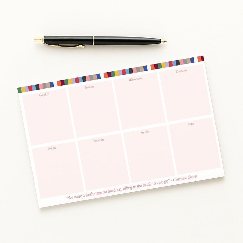 Weekly Notepad with eras colorful stripes at the top and a pen on a white background